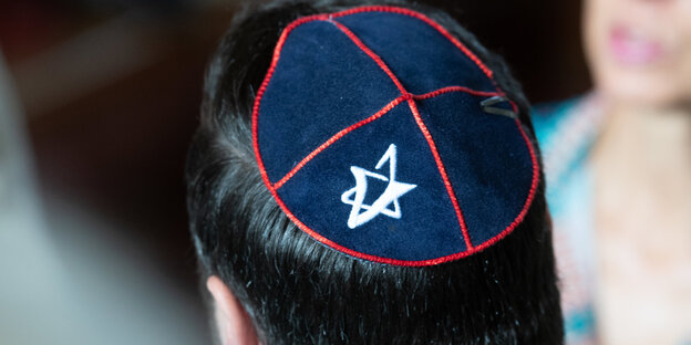 Ein Mann ist von hinten zu sehen, er trägt eine dunkelblaue Kippa mit roten Nähten und einem weißen Stern Ein Mann ist von hinten zu sehen, er trägt eine dunkelblaue Kippa mit roten Nähten und einem weißen Stern
