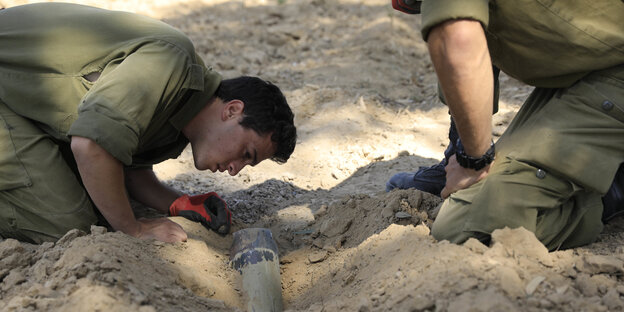 Zwei israelische Soldaten untersuchen eine Rakete, die sich in den Sandboden gebohrt hat Zwei israelische Soldaten untersuchen eine Rakete, die sich in den Sandboden gebohrt hat
