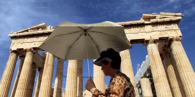 Vor der Akropolis in Athen steht eine Touristin mit Sonnenschirm