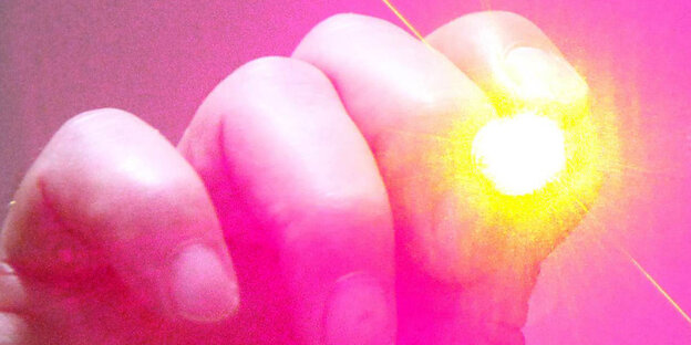 Eine Hand hält einen Laserpointer, aus dem grelles Licht kommt Eine Hand hält einen Laserpointer, aus dem grelles Licht kommt