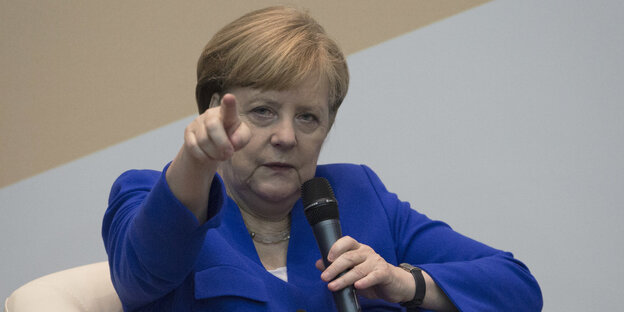 Angela Merkel sitzt zurückgelehnt in einem Sessel und zeigt mit dem rechten Zeigefinger nach vorne Angela Merkel sitzt zurückgelehnt in einem Sessel und zeigt mit dem rechten Zeigefinger nach vorne