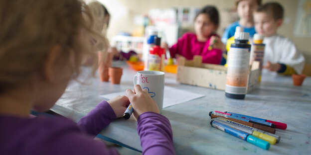 Ein Kind sitzt mit anderen Kindern an einem Tisch und malt Ein Kind sitzt mit anderen Kindern an einem Tisch und malt