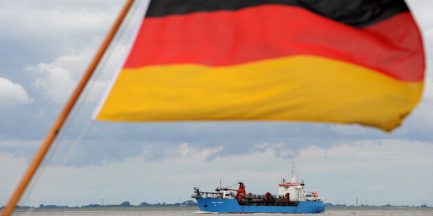 Ein Schiff fährt hinter einer Deutschlandflagge einen Fluss hinunter Ein Schiff fährt hinter einer Deutschlandflagge einen Fluss hinunter