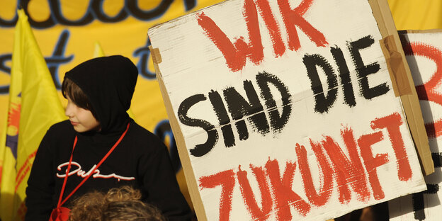 Ein Kind mit schwarzer Kapuze neben einem Transpi auf dem steht: Wir sind die Zukunft Ein Kind mit schwarzer Kapuze neben einem Transpi auf dem steht: Wir sind die Zukunft