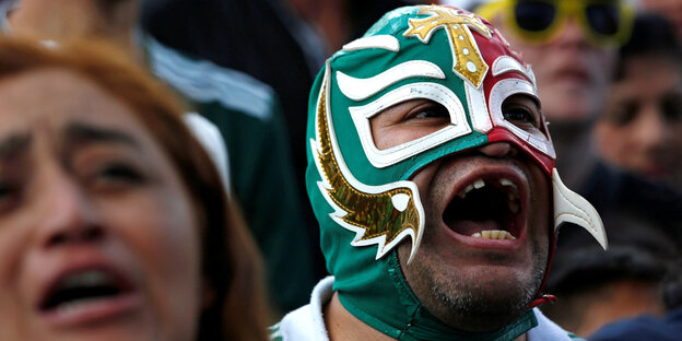 Ein mexikanischer Fan mit Fan-Maske jubelt in Mexiko City. Ein mexikanischer Fan mit Fan-Maske jubelt in Mexiko City.