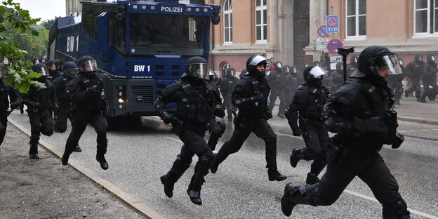 Behelmte Polizisten laufen beim G20-Gipfel neben einem Waserwerfer. Behelmte Polizisten laufen beim G20-Gipfel neben einem Waserwerfer.