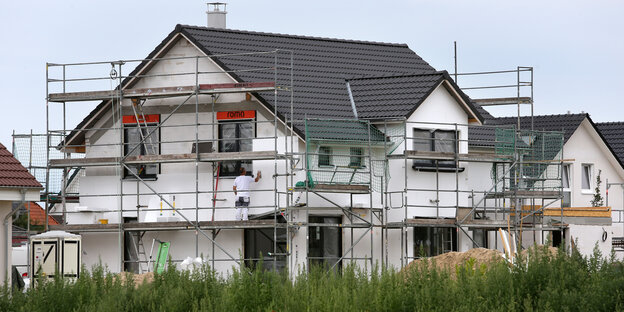 Ein Bauarbeiter steht an einer Hauswand eines Neubauprojekts Ein Bauarbeiter steht an einer Hauswand eines Neubauprojekts