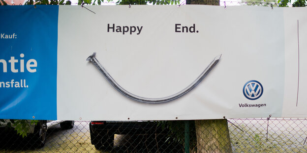 Ein Zaun, an dem ein VW-Plakat mit der Aufschrift "Happy End" hängt Ein Zaun, an dem ein VW-Plakat mit der Aufschrift "Happy End" hängt