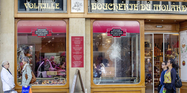 Ein gesprungenes Schaufenster einer Metzgerei, davor Passanten