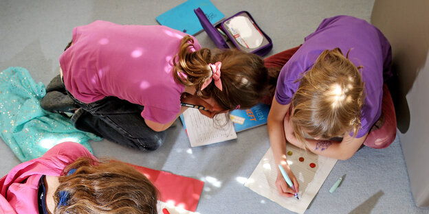 Drei Kinder hocken am Boden und schreiben in Schulhefte Drei Kinder hocken am Boden und schreiben in Schulhefte