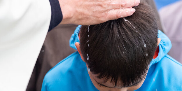Ein Priester gießt einem Jungen Wasser über den Kopf Ein Priester gießt einem Jungen Wasser über den Kopf