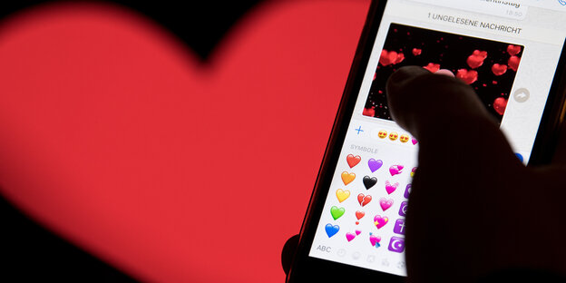 Ein rotes Herz im Hintergrund. Im Vordergrund ein Smartphone mit vielen Herz-Emojis drauf Ein rotes Herz im Hintergrund. Im Vordergrund ein Smartphone mit vielen Herz-Emojis drauf