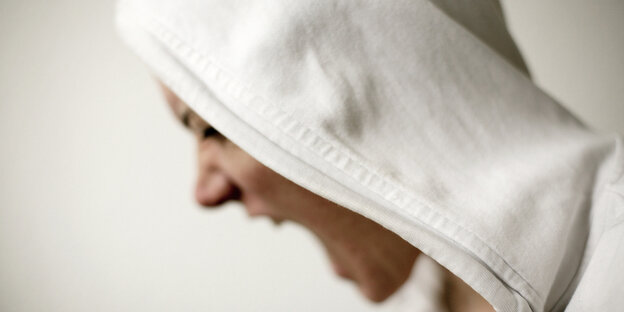 Ein Mensch mit einem weißen Kapuzenpulli ist von der Seite zu sehen. Er schreit Ein Mensch mit einem weißen Kapuzenpulli ist von der Seite zu sehen. Er schreit