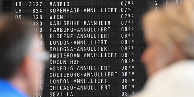 Zwei Reisende blicken auf eine Anzeigetafel am Flughafen, auf der zahlreiche annullierte Flüge stehen Zwei Reisende blicken auf eine Anzeigetafel am Flughafen, auf der zahlreiche annullierte Flüge stehen