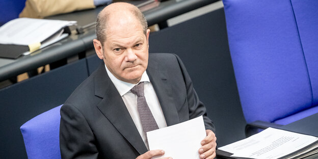 Der Bundesfinanzminister Olaf Scholz sitzt im Plenum des Bundestags und hält Papiere in der Hand Der Bundesfinanzminister Olaf Scholz sitzt im Plenum des Bundestags und hält Papiere in der Hand
