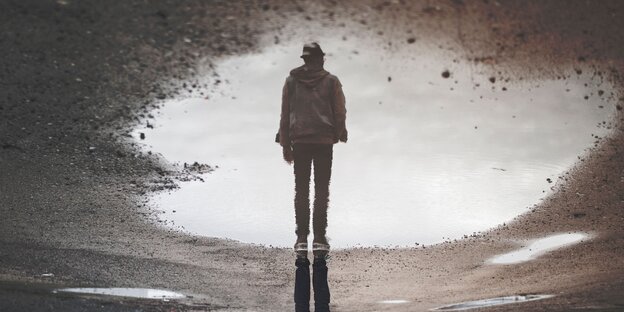 Die Reflektio eines Mannes mit Hut in einer Pfütze, im unteren Bildbereich sind, auf dem Kopf stehend, seine echten Beine zu sehen Die Reflektio eines Mannes mit Hut in einer Pfütze, im unteren Bildbereich sind, auf dem Kopf stehend, seine echten Beine zu sehen