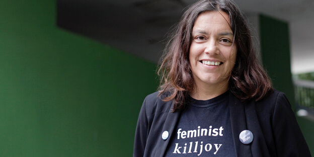 Sarah Ahmed steht vor einer grünen Wand und lächelt. Auf ihrem blauen T-Shirt steht in weißer Schrift „feminist killjoy“. Sarah Ahmed steht vor einer grünen Wand und lächelt. Auf ihrem blauen T-Shirt steht in weißer Schrift „feminist killjoy“.