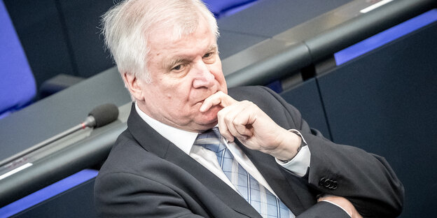 Horst Seehofer sitzt, er hält einen Finger an seinen Mund