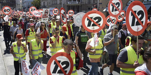 Demonstranten laufen im Protest gegen den Zwölf-Stunden-Tag mit Schildern durch Wien, auf denen eine 12 durchgestrichen ist Demonstranten laufen im Protest gegen den Zwölf-Stunden-Tag mit Schildern durch Wien, auf denen eine 12 durchgestrichen ist