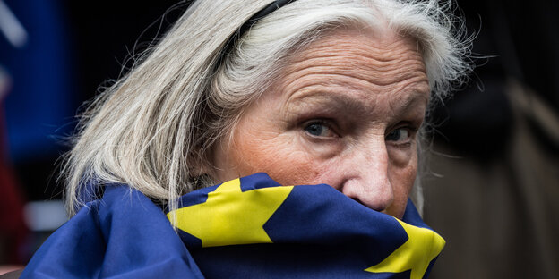 Nahaufnahme einer Frau, sie trägt eine Europaflagge als Schal, die ihr Gesicht halb verhüllt Nahaufnahme einer Frau, sie trägt eine Europaflagge als Schal, die ihr Gesicht halb verhüllt