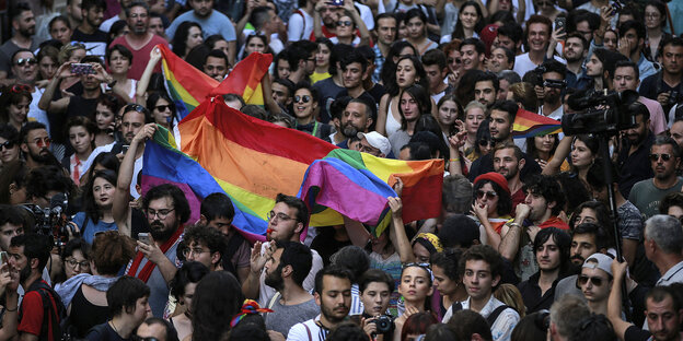 Viele Menschen stehen beieinander. Sie tragen eine bunte Flagge. Viele Menschen stehen beieinander. Sie tragen eine bunte Flagge.