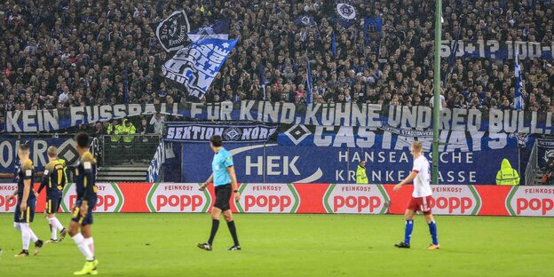 Fans im Volksparkstadion halten ein Plakat, das sich gegen Kühne wendet