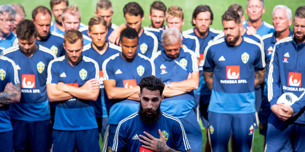 viele Spieler in blauen Trikots stehen auf dem Rasen, vor ihnen einer mit Bart, es ist Jimmy Durmaz viele Spieler in blauen Trikots stehen auf dem Rasen, vor ihnen einer mit Bart, es ist Jimmy Durmaz