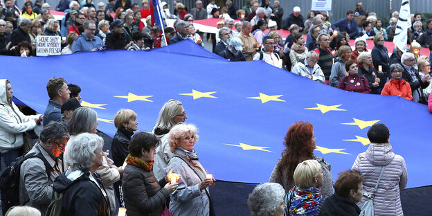 Rund um eine große EU-Flagge stehen Demonstrantinnen und Demonstranten mit Kerzen Rund um eine große EU-Flagge stehen Demonstrantinnen und Demonstranten mit Kerzen