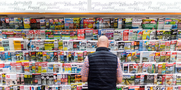 Ein Mann steht vor einem Zeitschriftenregal mit großer Auswahl Ein Mann steht vor einem Zeitschriftenregal mit großer Auswahl