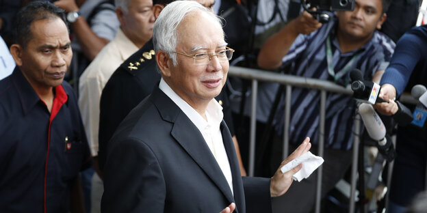 Najib Razak hebt leicht die Hände, an einem Gitter steht ein Kameramann Najib Razak hebt leicht die Hände, an einem Gitter steht ein Kameramann