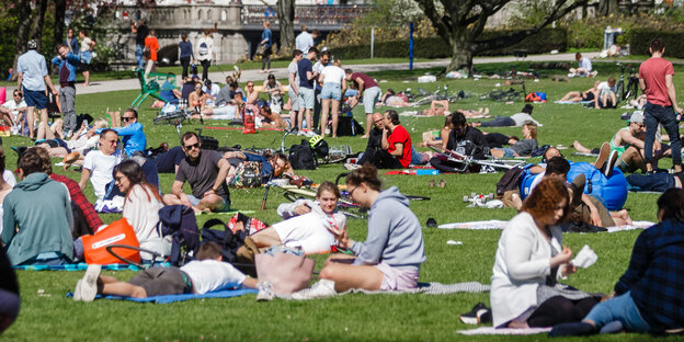 Menschen sitzen auf Decken und Jacken auf dem Boden einer Grünanlage Menschen sitzen auf Decken und Jacken auf dem Boden einer Grünanlage