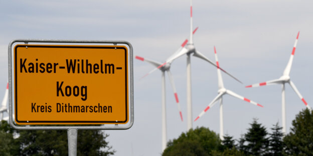 Ein Ortsschild, dahinter Häuser und Windräder Ein Ortsschild, dahinter Häuser und Windräder
