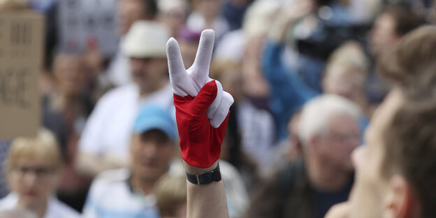 Eine Hand formt das Victory-Zeichen. Im Hintergrund sind viele Menschen Eine Hand formt das Victory-Zeichen. Im Hintergrund sind viele Menschen