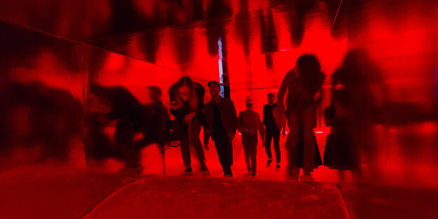 Spiegelnde Wände, rotes Licht, gewellter Boden: geduckt bewegen sich Besucher durch die Installation. Spiegelnde Wände, rotes Licht, gewellter Boden: geduckt bewegen sich Besucher durch die Installation.