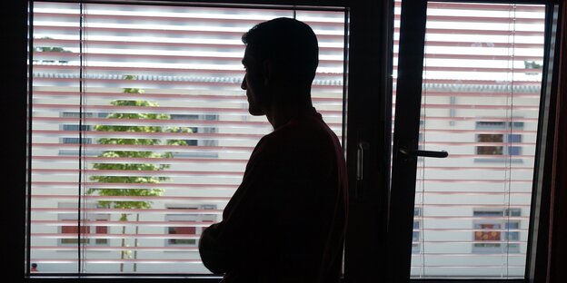 Die dunkle Silhouette eines Mannes an einem Fenster, vor dem ein Rollo herabgelassen ist Die dunkle Silhouette eines Mannes an einem Fenster, vor dem ein Rollo herabgelassen ist
