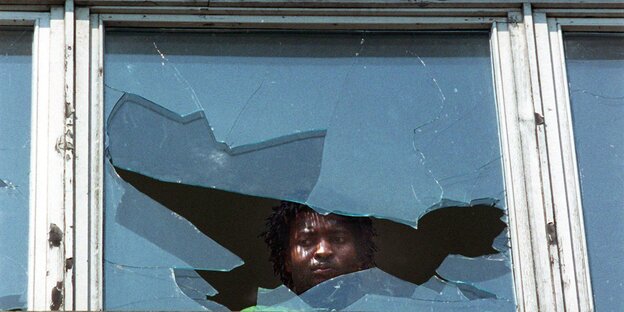 Ein schwarzer Mann schaut aus einem zerbrochenen Fenster Ein schwarzer Mann schaut aus einem zerbrochenen Fenster