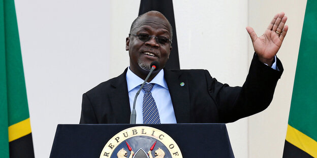 Tansanias Präsident John Magufuli steht ein einem Rednerpult mit dem Logo von Kenia und hebt beim Reden die linke Hand Tansanias Präsident John Magufuli steht ein einem Rednerpult mit dem Logo von Kenia und hebt beim Reden die linke Hand
