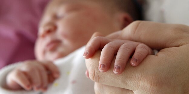 Ein neugeborenes Baby hält die Hand eines Erwachsenes. Das Gesicht des Babys ist unscharf im Hintergrund zu erkennen. Ein neugeborenes Baby hält die Hand eines Erwachsenes. Das Gesicht des Babys ist unscharf im Hintergrund zu erkennen.