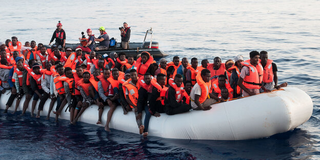 Geflüchtete sitzen mit Rettungswesten auf einem Schlauchboot Geflüchtete sitzen mit Rettungswesten auf einem Schlauchboot