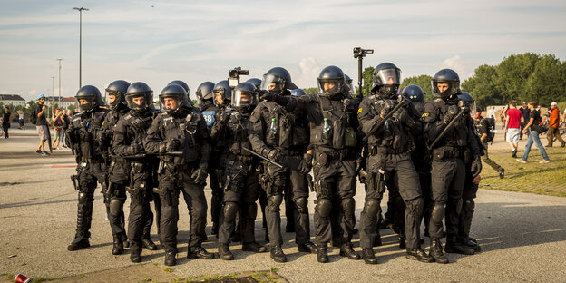 Polizisten mit Schutzkleidung und Helmen stehen dicht beieinander. Polizisten mit Schutzkleidung und Helmen stehen dicht beieinander.