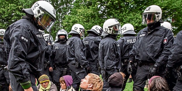 Menschen sitzten vor Polizisten, die in voller Montur sind Menschen sitzten vor Polizisten, die in voller Montur sind