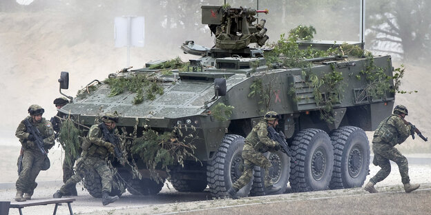 Nato-Soldaten laufen auf einem Truppenübungsplatz um einen Panzer Nato-Soldaten laufen auf einem Truppenübungsplatz um einen Panzer