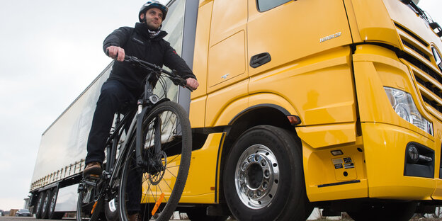 Ein Fahrradfahrer steht neben einem gelben LKW Ein Fahrradfahrer steht neben einem gelben LKW