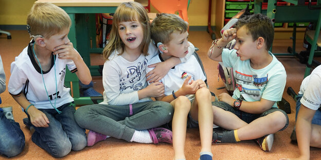 Vier Kinder sitzen nebeneinander, spielen und kommunizieren über Gebärdensprache Vier Kinder sitzen nebeneinander, spielen und kommunizieren über Gebärdensprache