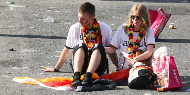 Zwei Fans sitzen nach dem Public Viewing zur WM-Vorrunde Südkorea - Deutschland auf dem Boden. Zwei Fans sitzen nach dem Public Viewing zur WM-Vorrunde Südkorea - Deutschland auf dem Boden.