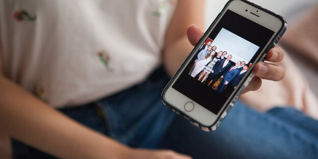 Eine Frau zeigt ein Bild auf dem Smartphone, auf dem eine Gruppe Menschen zu sehen sind Eine Frau zeigt ein Bild auf dem Smartphone, auf dem eine Gruppe Menschen zu sehen sind