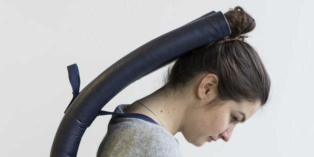 Eine Frau trägt eine Art futuristischen Rucksack, der ihren Kopf nach vorne beugt Eine Frau trägt eine Art futuristischen Rucksack, der ihren Kopf nach vorne beugt