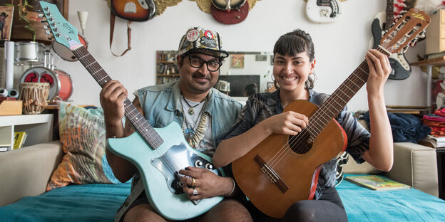 Die Musiker Arish Ahmad Khan und Saba Lou Khan sitzen mit Gitarren in den Händen auf einem Sofa Die Musiker Arish Ahmad Khan und Saba Lou Khan sitzen mit Gitarren in den Händen auf einem Sofa