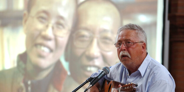 Gedenken für Liu Xiaobo in Berlin: Vorne ein Mann mit Gitarre, es ist Wolf Biermann, hinter ihm ein Foto von Liu Xia und Liu Xiaobo Gedenken für Liu Xiaobo in Berlin: Vorne ein Mann mit Gitarre, es ist Wolf Biermann, hinter ihm ein Foto von Liu Xia und Liu Xiaobo
