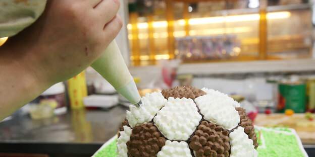 Ein Konditor verziert eine Torte, die wie ein Ball aussieht Ein Konditor verziert eine Torte, die wie ein Ball aussieht